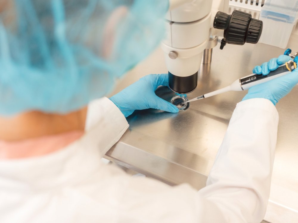 Lab technician pipetting a sample under a microscope
